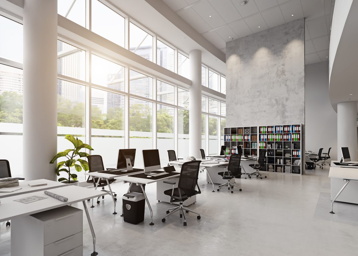 An open-plan office with a white floor, rows of desks and floor-to-ceiling windows