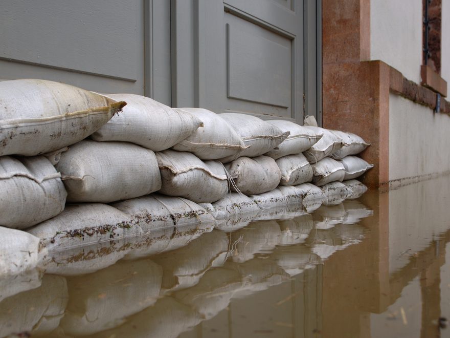 Sandbags stacked across a doorway, with floodwater reflecting the wall behind them